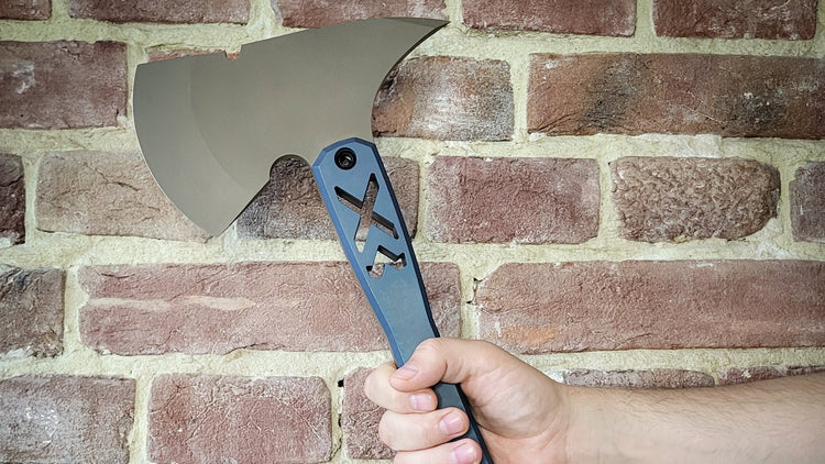 Hand holding a blue and silver axe against a brick wall with 'CALTI' branding.